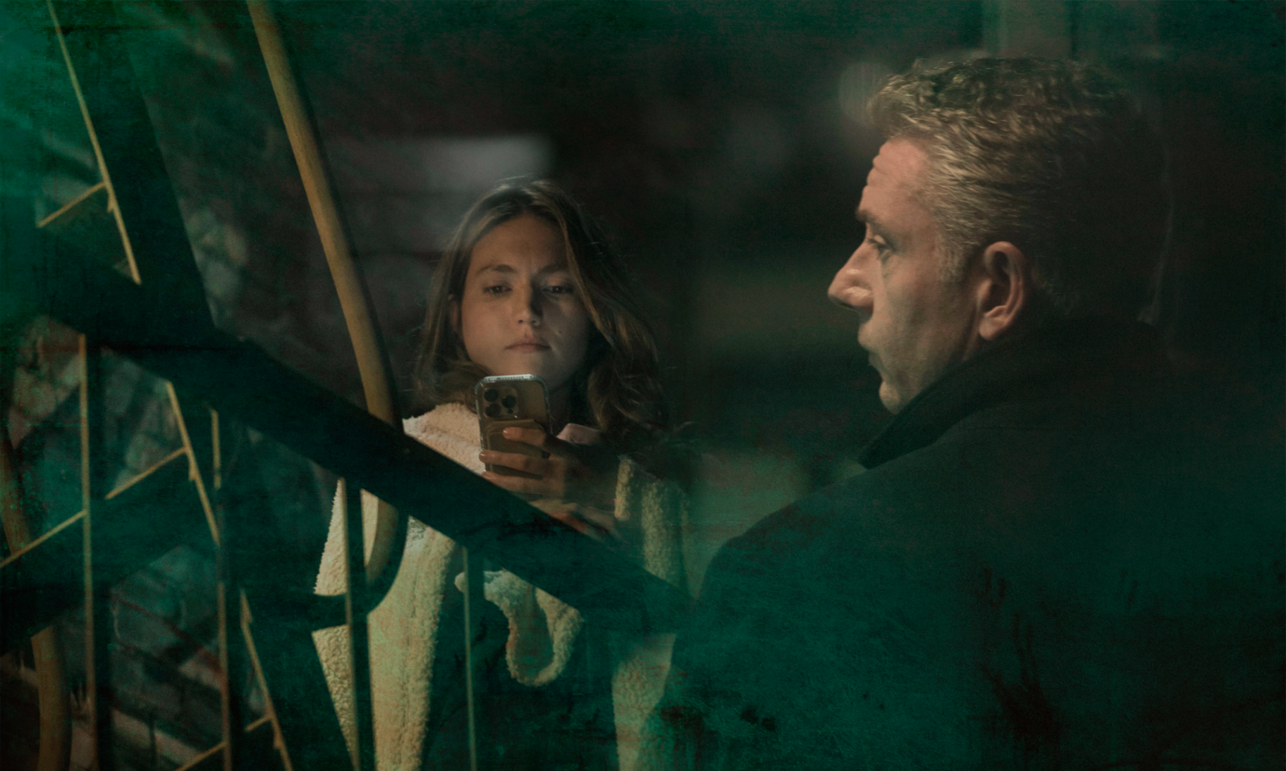 A young woman looks into her phone while an older man stands turned away — a still from The Most Honest Thing In The Room.