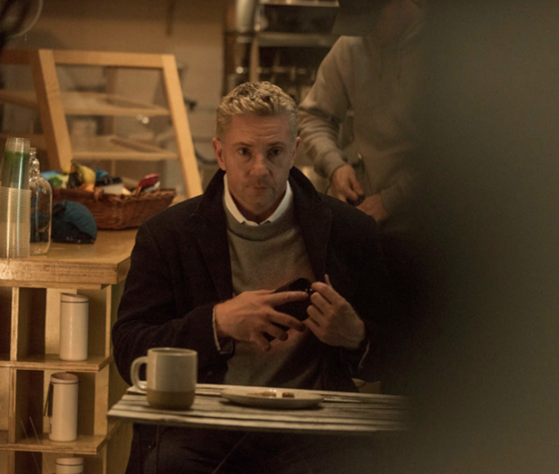 Tommy sits at a cafe table holding his phone.