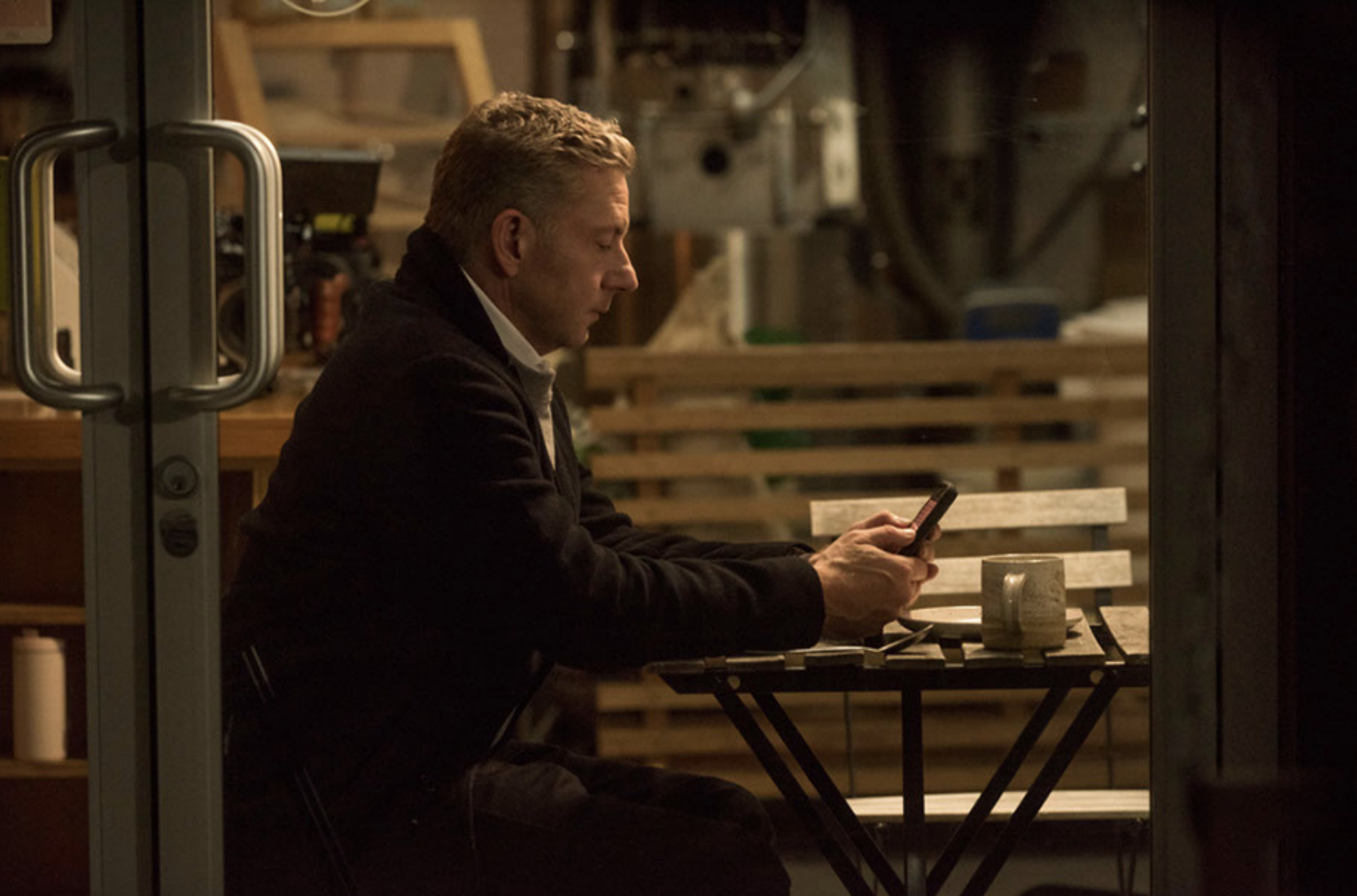 Tommy sits at a workshop table looking at his phone.